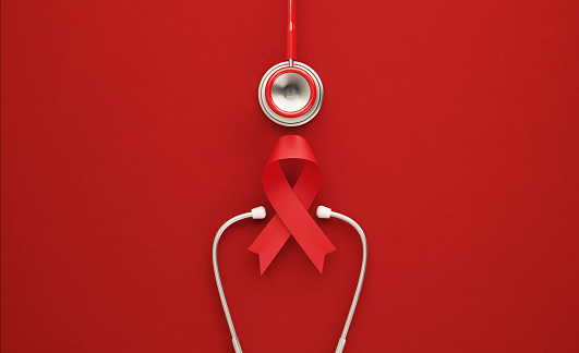 Red stethoscope and red AIDS awareness ribbon on red background. Horizontal composition with copy space. World AIDS Day concept.