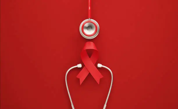 Red stethoscope and red AIDS awareness ribbon on red background. Horizontal composition with copy space. World AIDS Day concept.