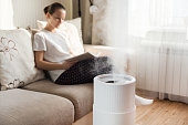 Modern air humidifier, aroma oil diffuser at home. Improving the comfort of living in a house, Improving the well-being. Ultrasonic steam technology. Woman reading book on background