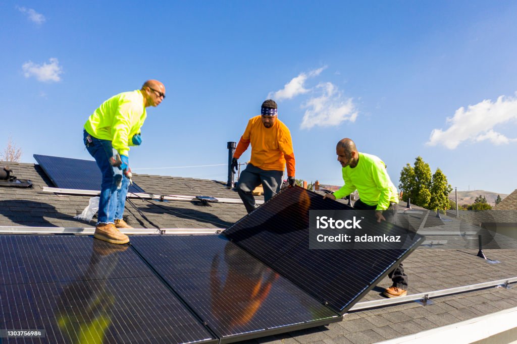 Team of Workers Installing Solar Panels on Residential Rooftop in California A team of workers installing solar panels on a home in Southern California Solar Panel Stock Photo