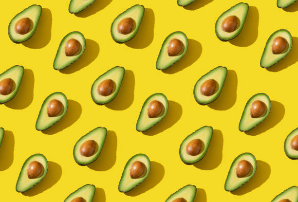 istock Avocado halves pattern with hard shadow and trendy lighting on yellow background 1303761036