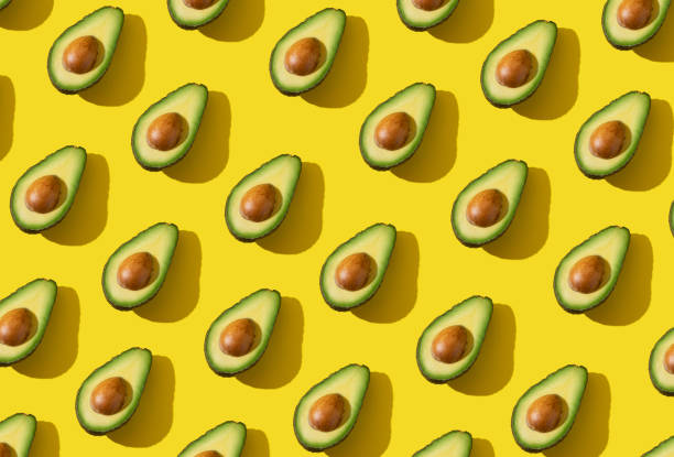 L'avocado dimezza il motivo con ombra dura e illuminazione alla moda su sfondo giallo - foto stock