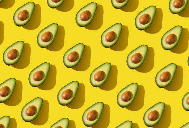 istock Avocado halves pattern with hard shadow and trendy lighting on yellow background 1303761037