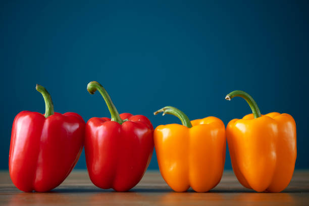 healthy organic vegetables, 4 colored bell peppers, arranged side by side on blue background