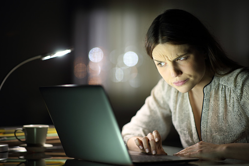 Mujer sospechosa revisando contenido de computadora portátil en la noche photo