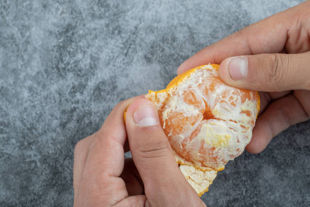istock Man hands peeling a fresh tangerine on a gray background 1303764883