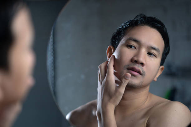 istock Asian man looking in the mirror at bathroom He touch his face 1303774349