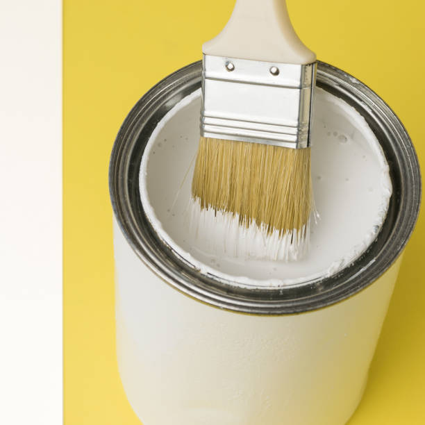 istock Brush inside a jar with white paint on a yellow and white background. 1303774961