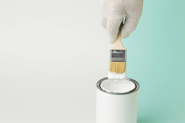 istock A brush with white paint in a man's hand on a blue and white background. 1303774965