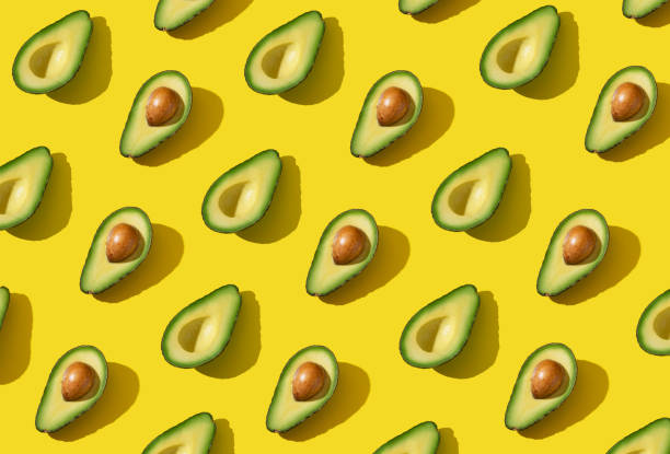 istock Avocado halves pattern with hard shadow and trendy lighting on yellow background 1303776665
