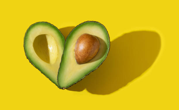 istock Avocado halves as heart shape with hard shadow on yellow background 1303779981