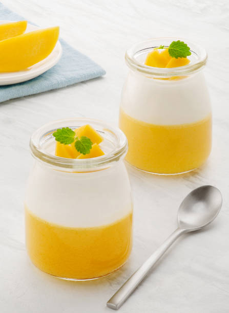 istock Sweet dessert of yogurt and mango with mint. Two jars with dessert on a light table 1303780588