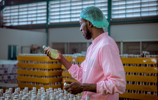 Worker of science in bottle beverage factory wearing safety  hat  working to packing and check drink machine conveyer belt before distribution to market business.