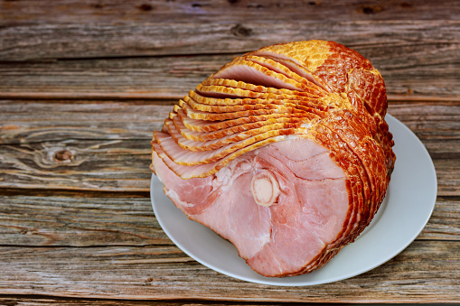 Close up of sliced honey smoked ham on wooden table. Copy space.