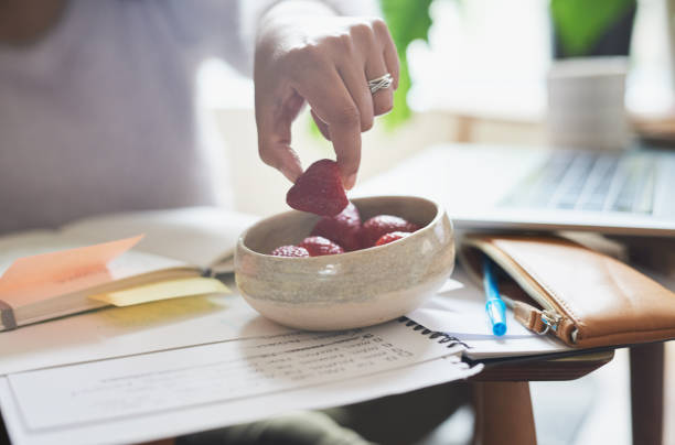 Closeup shot of an unrecognisable woman eating strawberries while working at home