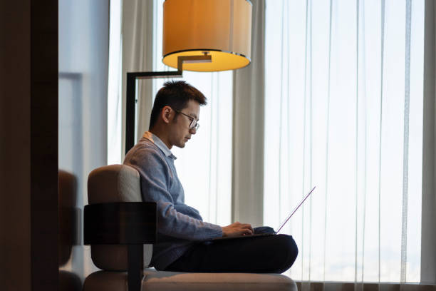 istock Asian man using laptop while working at home on bedroom sofa 1303790738