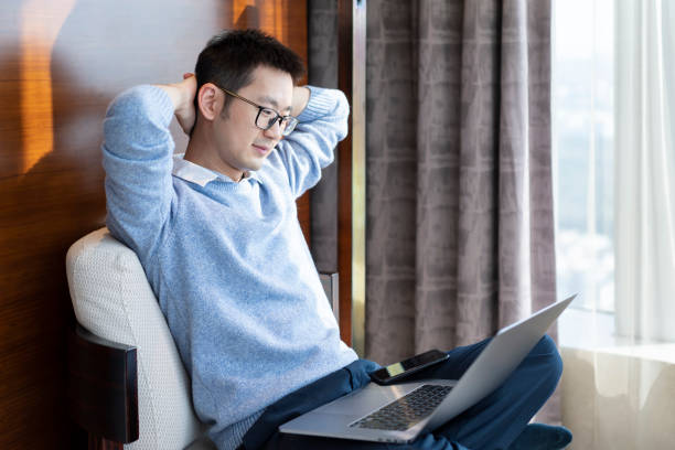istock Asian man using laptop while working at home on bedroom sofa 1303791883