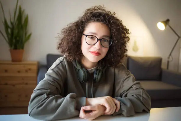 Photo of girl serious calm expression on her face in glasses is sitting at table at home. Video Conference or e-learning at home.