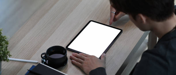 istock Horizontal image of young man using stylus pen writing on digital tablet while sitting in living room. 1303792909