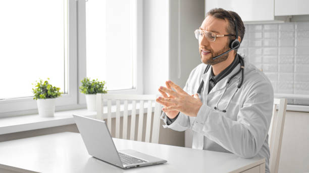 photo d’un docteur devant un moniteur d’ordinateur portatif. il conseille le client sur la communication vidéo. format 16:9 - colleague looking at camera indoors lifestyles photos et images de collection