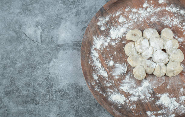 istock A wooden round board with uncooked dumplings and flour 1303797613