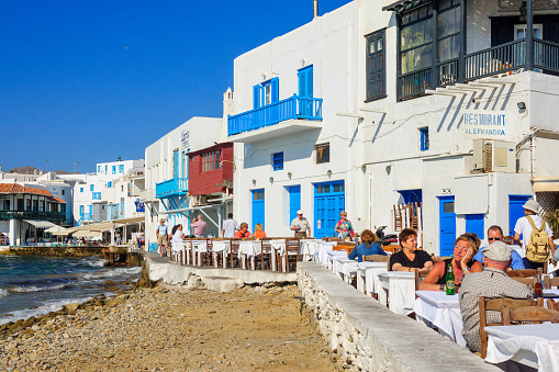 Mykonos, Greece - October 02, 2011: Village and beach restaurants scene, with little Venice houses, local businesses, locals and visitors, in Mykonos, Mykonos Island, Greece