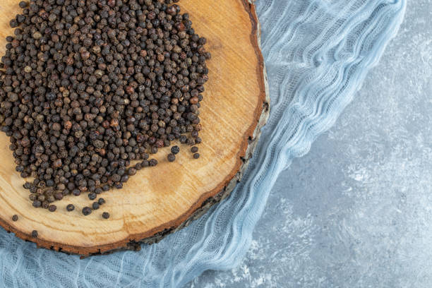 istock Black pepper grains on wooden piece with cloth 1303803109