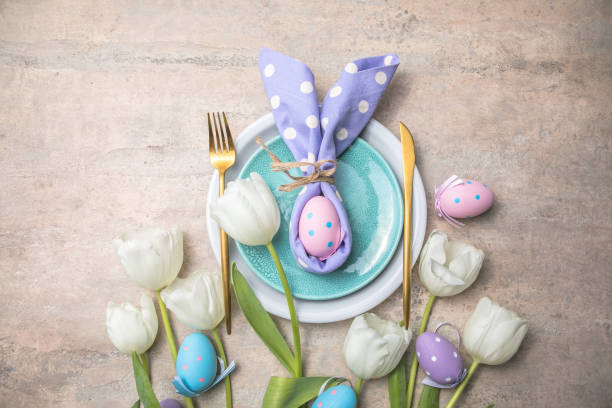 istock Easter holiday table setting with bunny  from egg on white plate and tulips flowers.  Gray concrete table, top view with copy space for text. Happy Easter background 1303804035