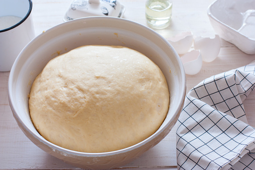Freshly cooked yeast dough in ceramic bowl on white wooden table, selective focus