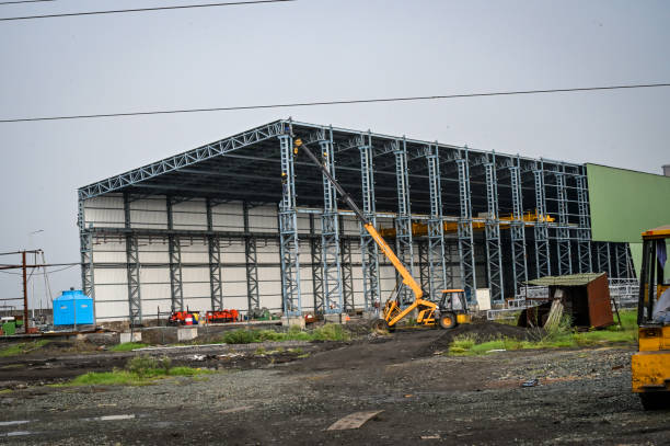 Two industrial warehouse buildings with aluminium roof eaves and rainwater drainage pipelines on white concrete wall against blue clear sky background, perspective side view