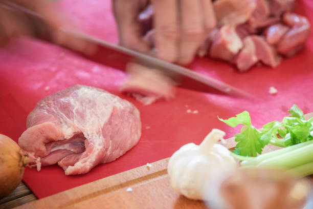Goulash, traditional Hungarian stew meal preparing, basic ingredients on table, cutting peace of meat using sharp knife, close-up, selective focus, motion blur at right hand