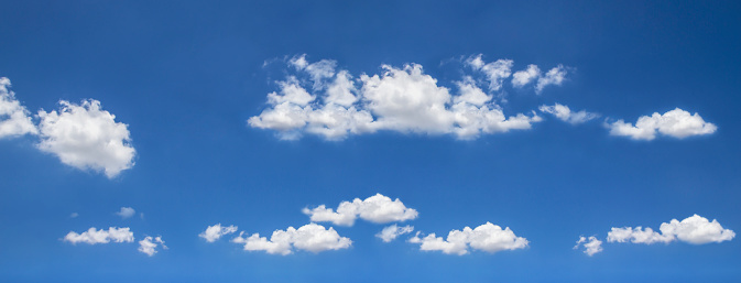 Panoramic view of a bright blue sky filled with fluffy white clouds. The clouds vary in size and are spread across the sky, suggesting a vast open atmosphere. The blue of the sky is a clear, vibrant hue that suggests a sunny day. There is a serene and tranquil quality to the scene, which may evoke feelings of calmness and openness.