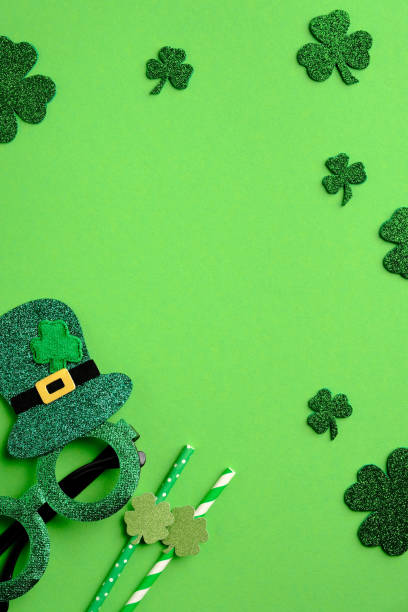 istock St Patricks day vertical banner design. Top view shamrock four leaf clover, Patricks day glasses, drinking straws on green background. Saint Patrick's day greeting card template 1303811021