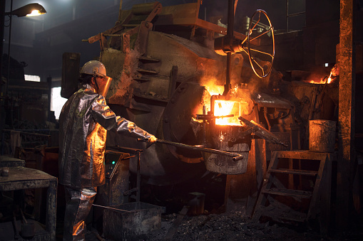Trabajador en fundición. Hombre de trabajo en traje de protección contra temperatura vertiendo metal líquido en el cubo. Producción de acero. photo
