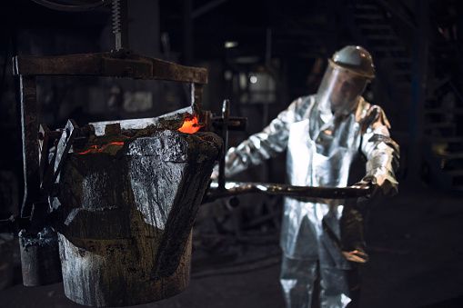 Trabajador de fundición en traje de fuego protector aluminizado empujando cubo con hierro líquido fundido en fundición. photo