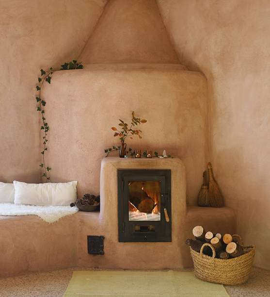 Charming inertia stove made of clay and pink plaster with lit fire and firewood basket Charming inertia stove made of clay and pink plaster with lit fire and firewood basket adobe oven stock pictures, royalty-free photos & images