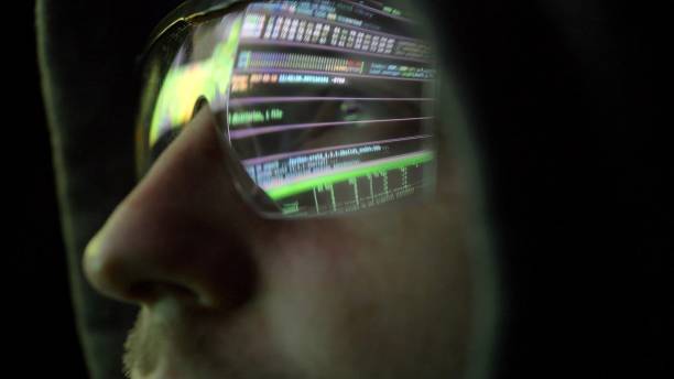 istock Hooded Hacker in Futuristic Glasses Looking at Computer Screen Code in Dark 1303813382