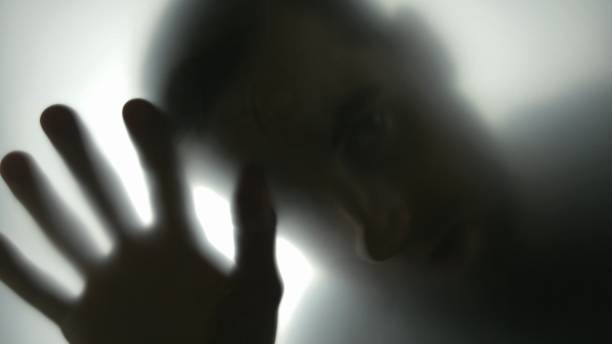 istock Silhouette of Disturbing Man Looking at Camera Through Translucent Glass 1303813430