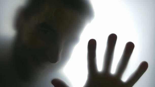istock Silhouette of Disturbing Man Looking at Camera Through Translucent Glass 1303813585