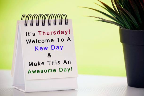 Inspirational quote on white paper stand with potted plant and blurred background - It is Thursday, welcome to a new day and make this an awesome day stock photo