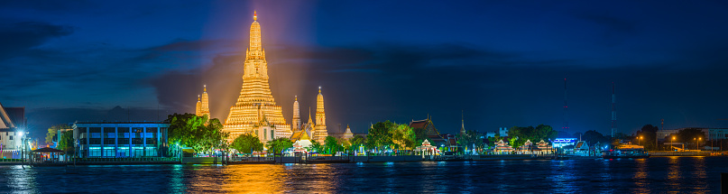 The iconic spire of Wat Arun spotlit against the blue dusk sky across the Chao Phraya River in the heart of Bangkok, Thailand’s vibrant capital city.
