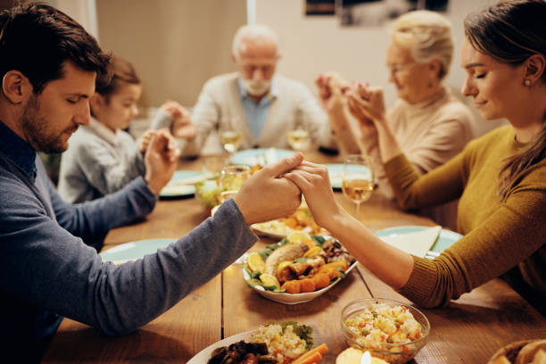 ダイニングテーブルで食事の前に恵みを言う拡張家族。 - praying saying grace dinner meal ストックフォトと画像