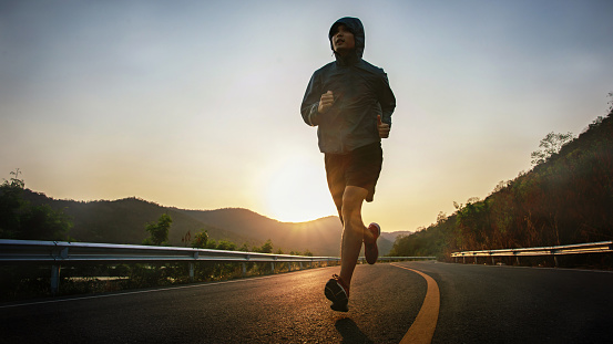 Full length shot of healthy young man running on the asphalt road in the morning