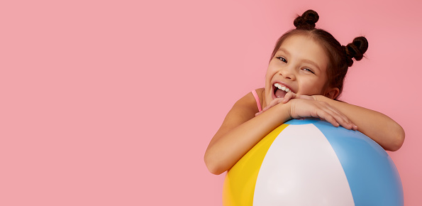 beautiful smiling little child girl with colorful beach ball on pink background. copy space for text