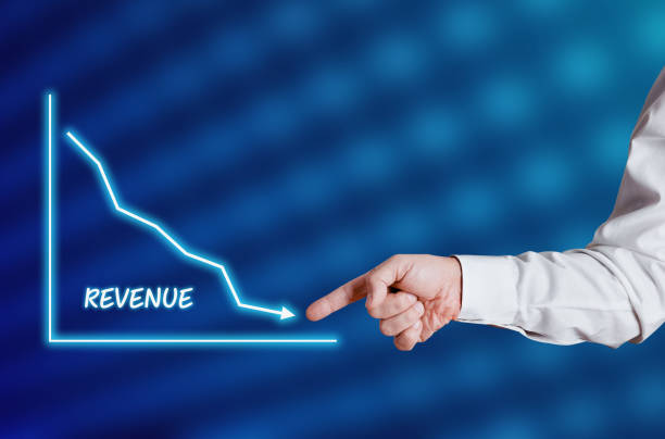 istock Businessman hand points to the word revenue with a decreasing chart or graph. 1303829090