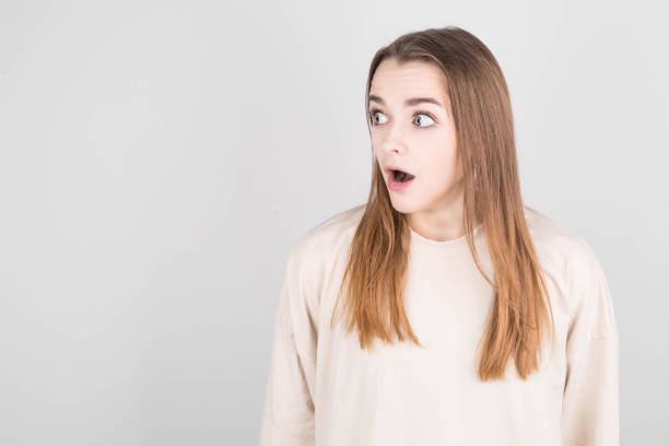 istock Image of surprised young lady standing isolated on gray background. Looking away 1303829892