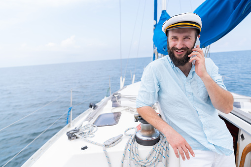 A man wearing a straw hat is driving a sailboat and enjoying it.