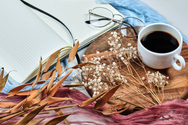 istock Open notebook, glasses, a cup of tea and dried plants on white desk 1303834515