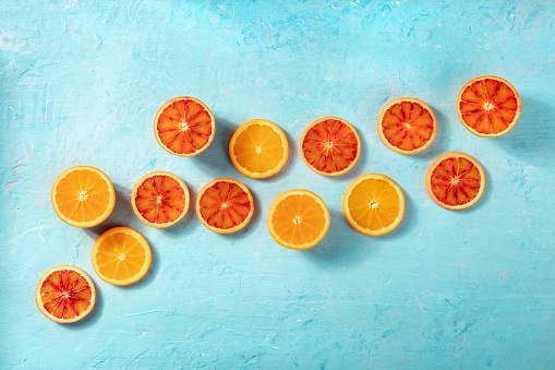 Blood oranges and regular oranges, overhead flat lay shot on a blue background with copy space. Summer banner