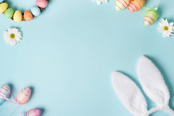 istock Easter frame with bunny ears, eggs, white flowers on pastel blue background. Top view. Happy Easter holiday. Greeting card. 1303841429